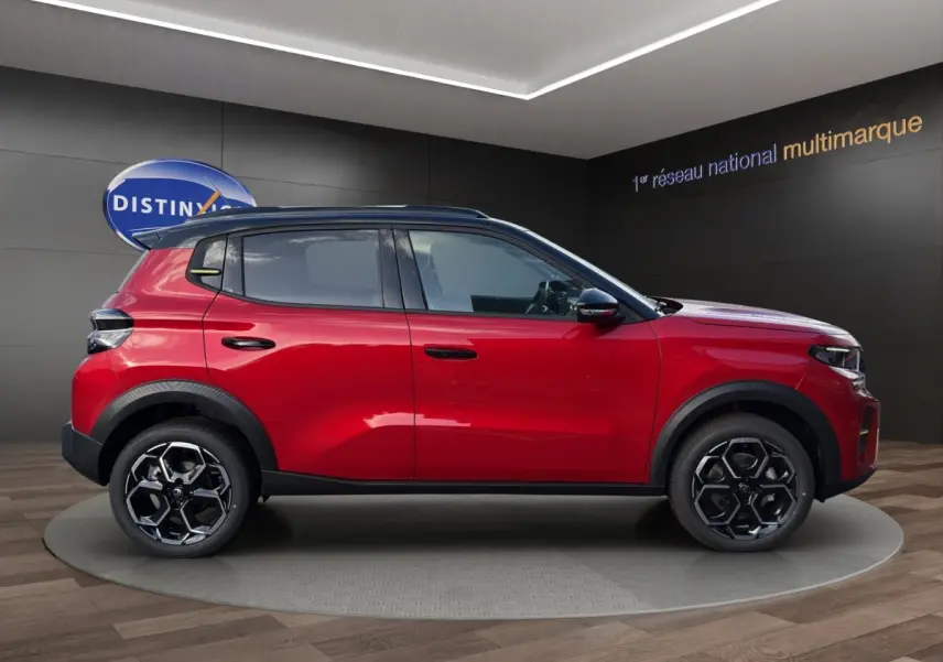 Profil côté gauche d'un Citroën C3 hybride rouge avec toit noir et jantes alliage au design hexagonal.