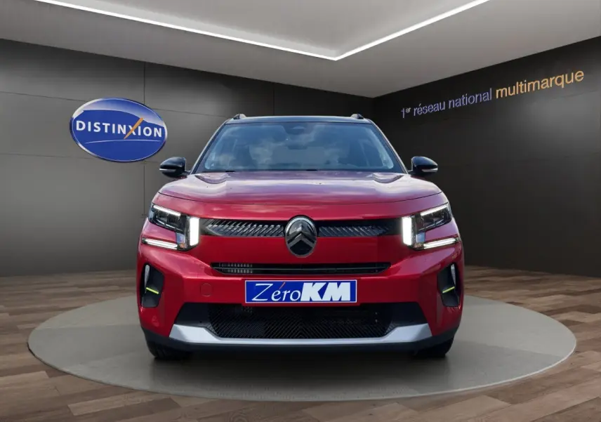 Vue avant d'une Citroën C3 hybride rouge avec phares LED et calandre noire brillante en showroom.