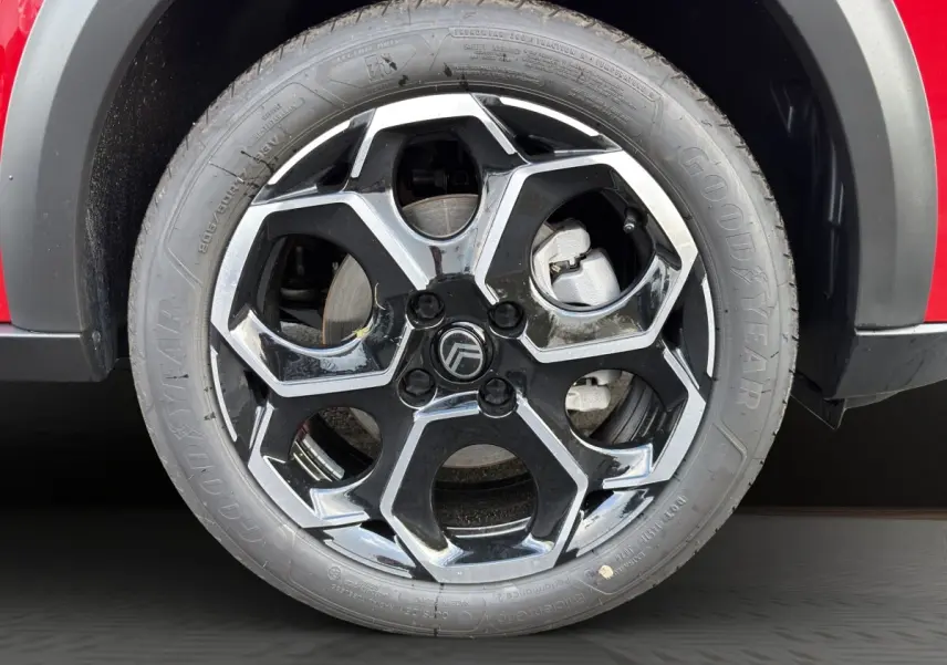 Gros plan sur la roue avant droite d’une Citroën C3 rouge avec jante alliage noire et argentée au design hexagonal.