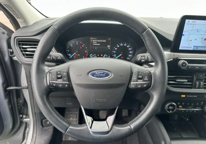 Vue intérieure centrée sur le volant cuir noir et le tableau de bord du Ford Kuga gris solaire 2020 avec écran tactile et commandes intégrées.