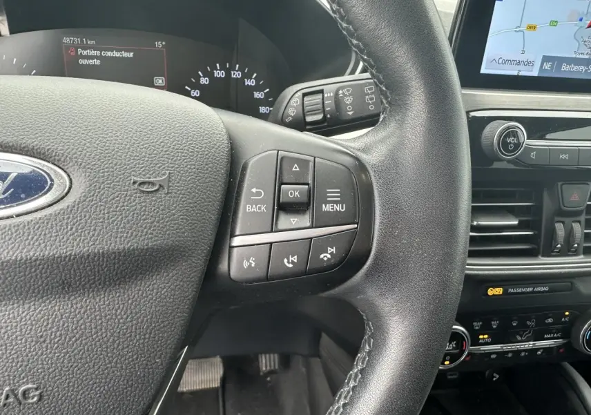 Gros plan sur le volant multifonction et le tableau de bord du Ford Kuga gris solaire avec écran tactile et commandes intégrées.