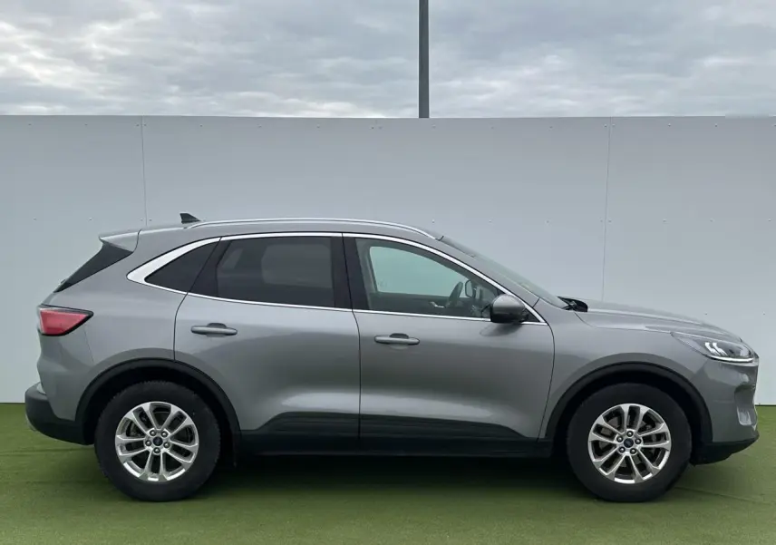 Vue de profil côté gauche du Ford Kuga III gris solaire avec barres de toit aluminium et vitres arrière surteintées.