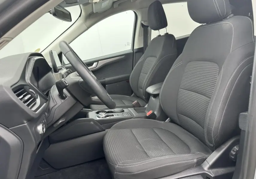 Vue intérieure côté conducteur du Ford Kuga gris solaire 2020, sièges tissu noir et console centrale avec sélecteur rotatif.