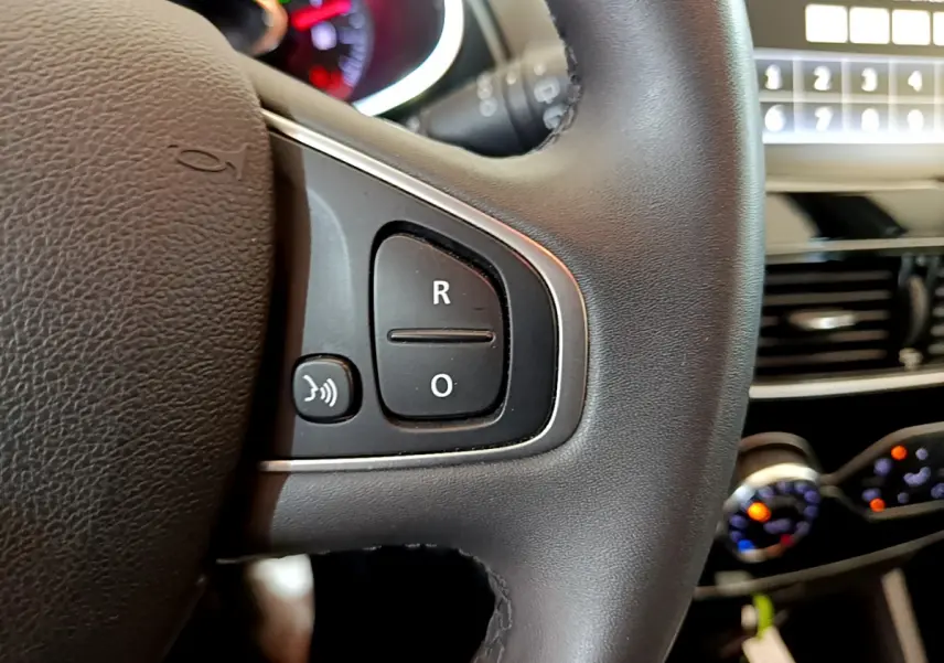 Gros plan sur les commandes du volant cuir noir de la Renault Clio Business TCe 90, avec tableau de bord et écran tactile en arrière-plan.