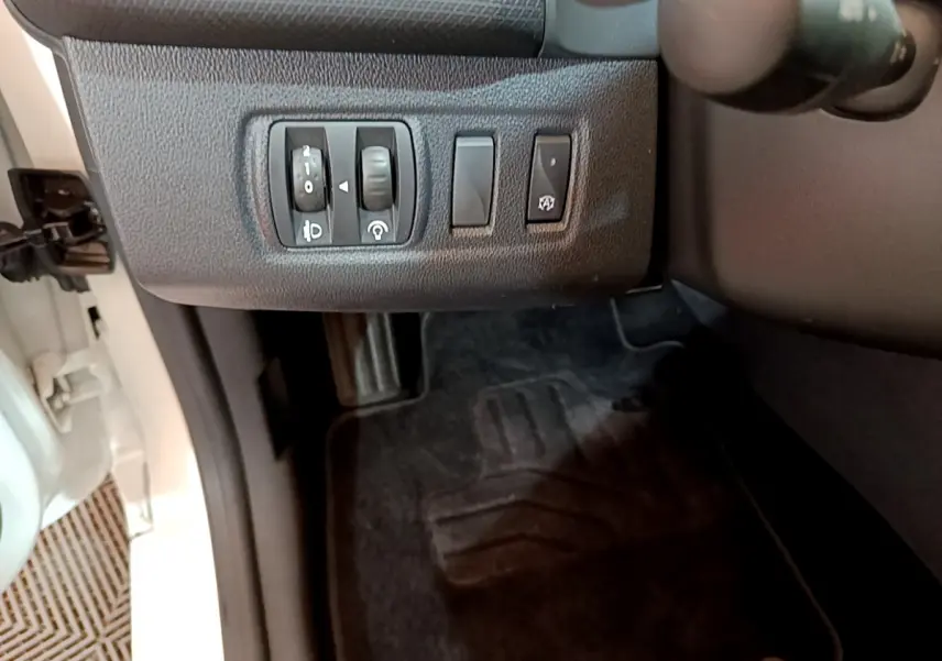 Vue intérieure côté gauche du tableau de bord de la Renault Clio Business TCe 90 blanche, avec commandes d'éclairage et réglages.