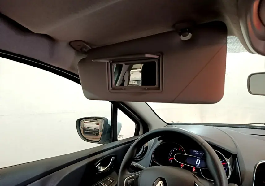 Vue intérieure côté conducteur de la Renault Clio Business blanche, volant cuir et pare-soleil avec miroir ouvert.