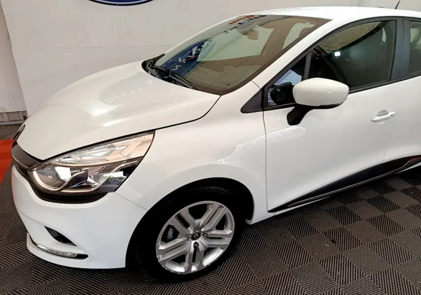 Renault Clio Business TCe 90 blanc vue 3/4 avant droit, phares LED et jantes alliage visibles sur fond intérieur.