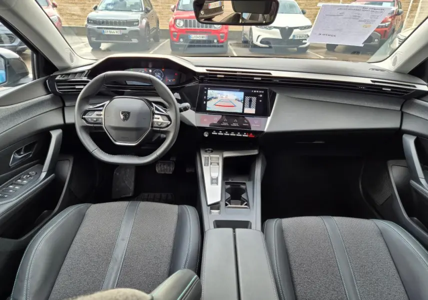 Vue intérieure avant du Peugeot 308 2024 bleu, montrant le volant compact, l’écran tactile avec caméra de recul et l’accoudoir central.