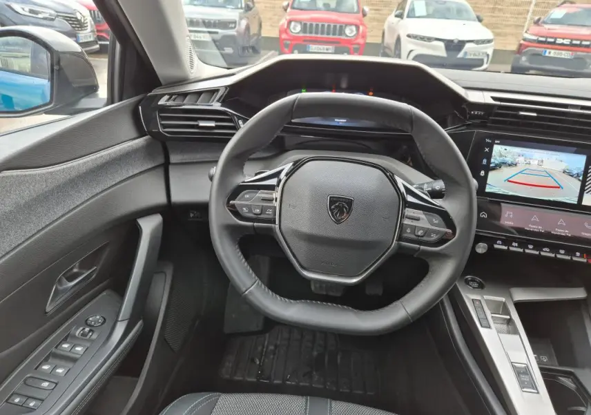 Vue intérieure centrée sur le volant et le tableau de bord numérique de la Peugeot 308 bleu avec caméra de recul affichée.