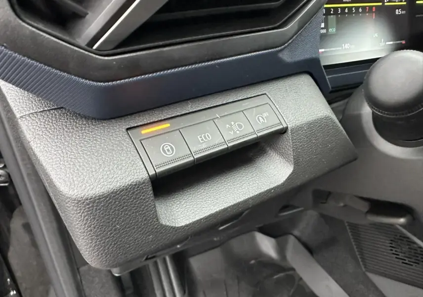 Gros plan sur les commandes de tableau de bord du Dacia Duster noir 2025, avec bouton ECO et indicateur lumineux orange.