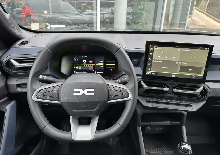 Vue intérieure frontale du tableau de bord noir du Dacia Duster 2025 avec volant multifonction et écran tactile central.