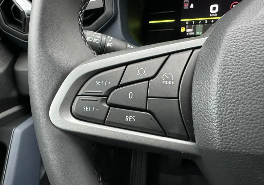 Gros plan sur les commandes de régulateur de vitesse à gauche du volant du Dacia Duster noir 2025.