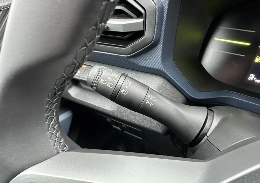 Gros plan sur la commande des feux et clignotants à gauche du volant dans le Dacia Duster noir 2025.