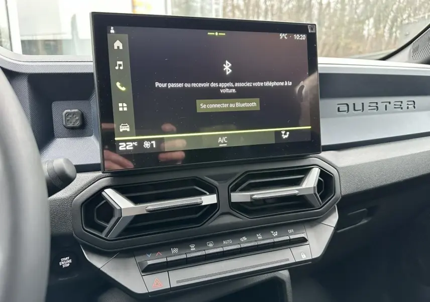 Vue intérieure du tableau de bord du Dacia Duster 2025 noir, avec écran tactile central et aérateurs hexagonaux.