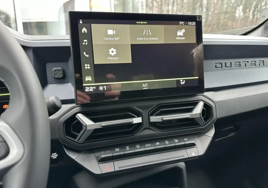 Vue intérieure du tableau de bord du Dacia Duster 2025 noir, avec écran tactile central et aérateurs hexagonaux.