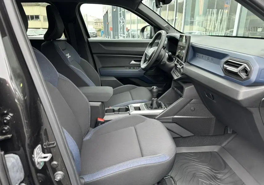 Vue intérieure côté conducteur du Dacia Duster noir 2025, montrant sièges tissu bicolore et tableau de bord moderne.