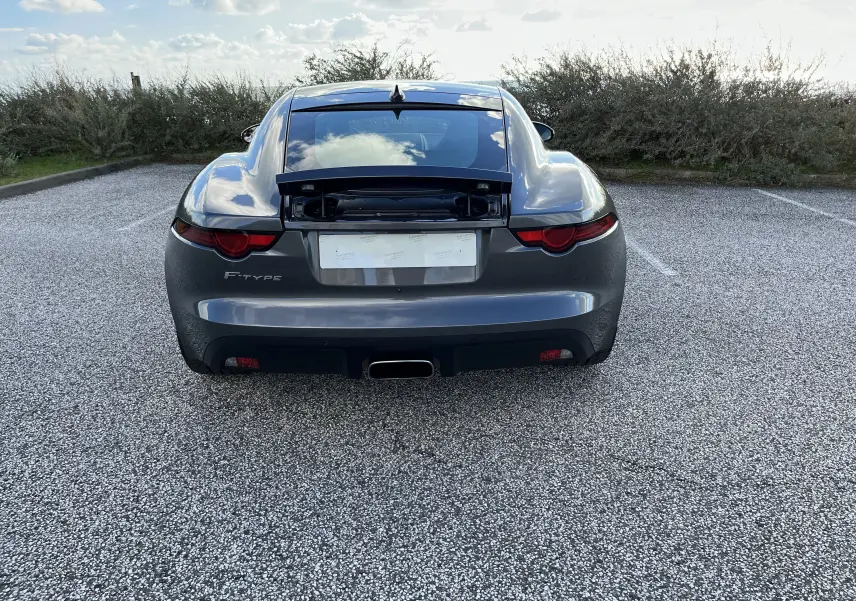 Vue arrière d'une Jaguar F-TYPE II Coupé 2.0T gris Corris avec coffre arrière ouvert et échappement central chromé.