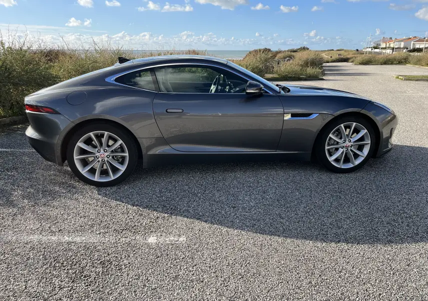 Vue de profil côté gauche d'une Jaguar F-TYPE II Coupé 2.0T 300 BVA8 gris Corris, avec jantes 19 pouces et lignes sportives élégantes.
