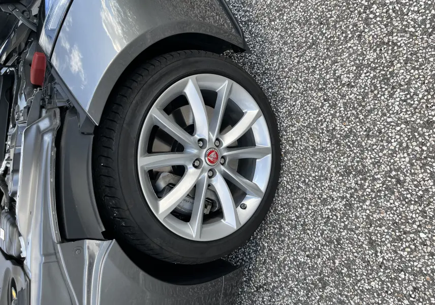 Gros plan sur la roue avant gauche de la Jaguar F-TYPE gris Corris, jante 19 pouces 10 branches avec logo Jaguar rouge.