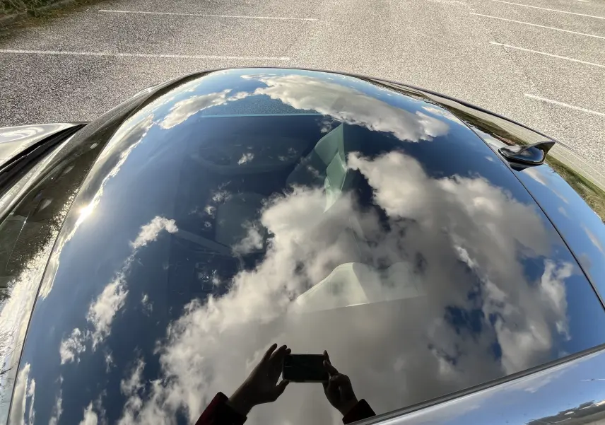 Vue plongeante sur le toit vitré d'une Jaguar F-TYPE gris Corris, reflétant un ciel nuageux et l'intérieur cuir clair visible.