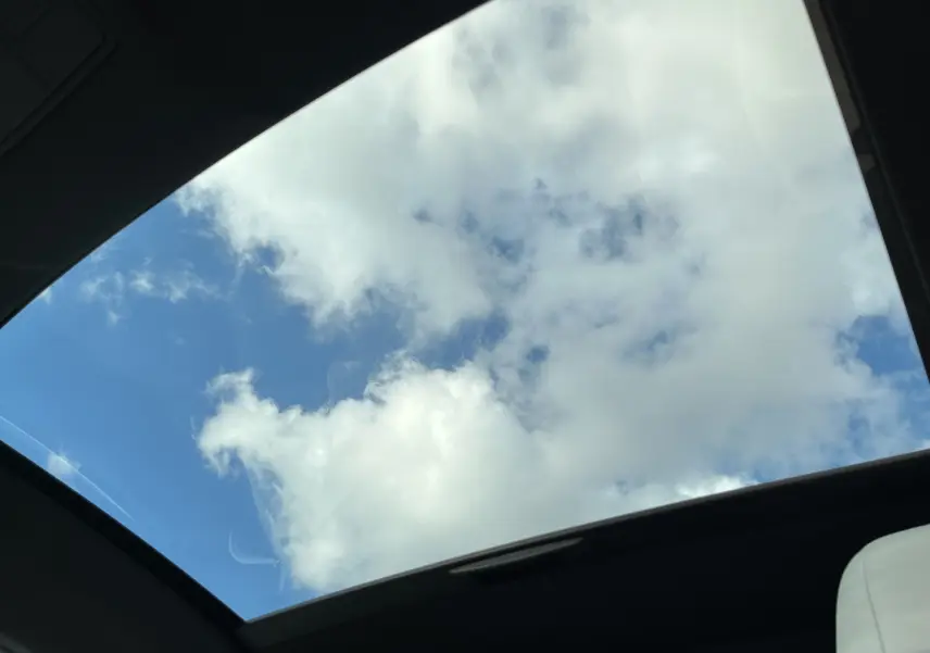 Vue intérieure du toit ouvrant panoramique de la Jaguar F-TYPE II Coupé 2.0T 300 BVA8, ciel bleu avec nuages visibles.