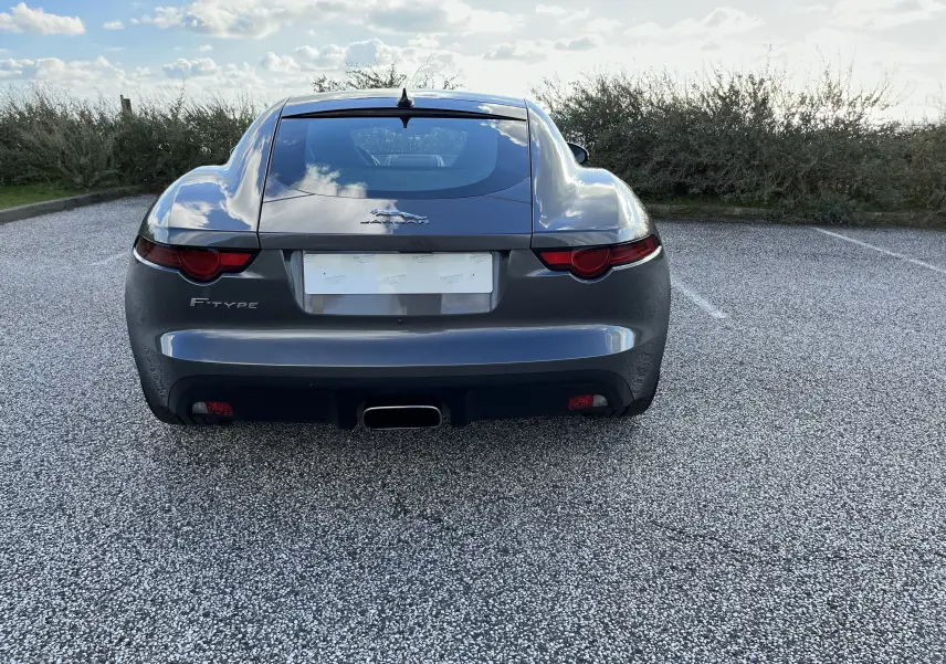 Vue arrière d'une Jaguar F-TYPE II Coupé 2.0T 2018 en gris Corris, avec échappement sport central et feux arrière ronds.