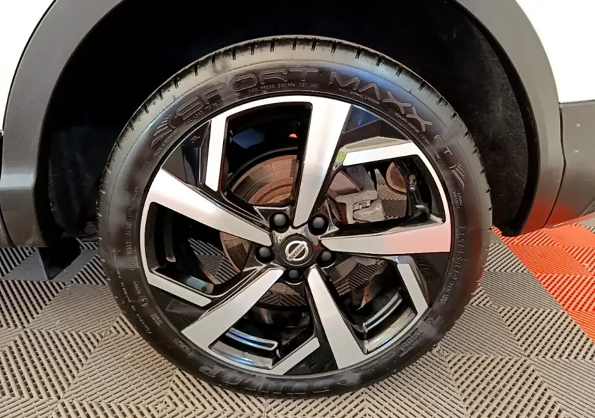 Gros plan sur la roue avant droite du Nissan Qashqai blanc, mettant en valeur la jante alliage bicolore moderne.