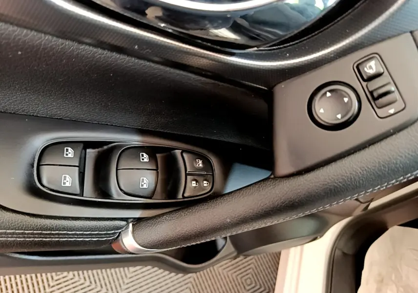 Gros plan sur la porte côté conducteur du Nissan Qashqai blanc, montrant les commandes des vitres et rétroviseurs.