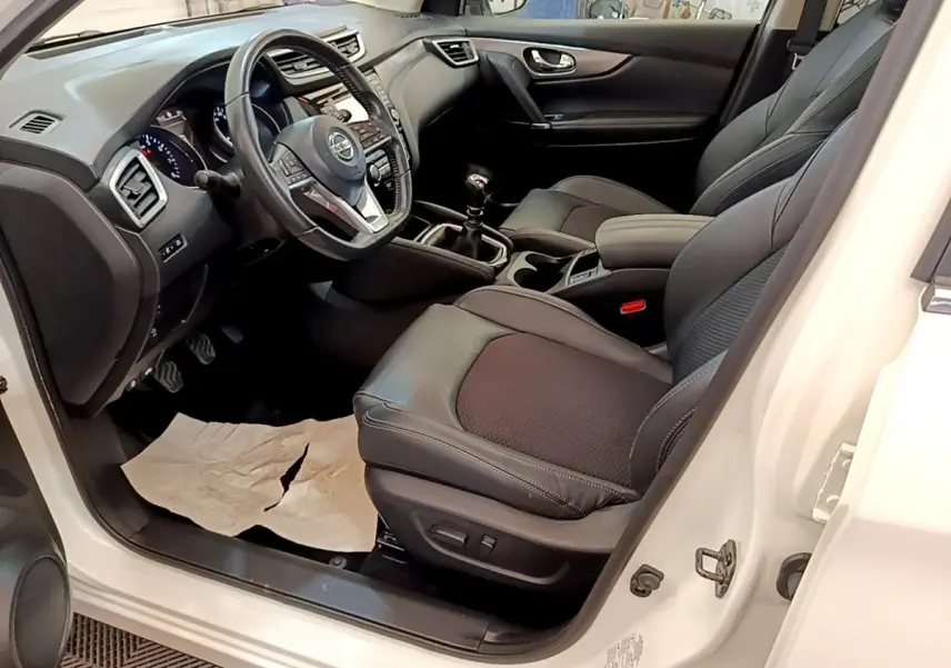 Vue intérieure côté conducteur du Nissan Qashqai blanc 2019, avec sièges cuir noirs et volant multifonctions.