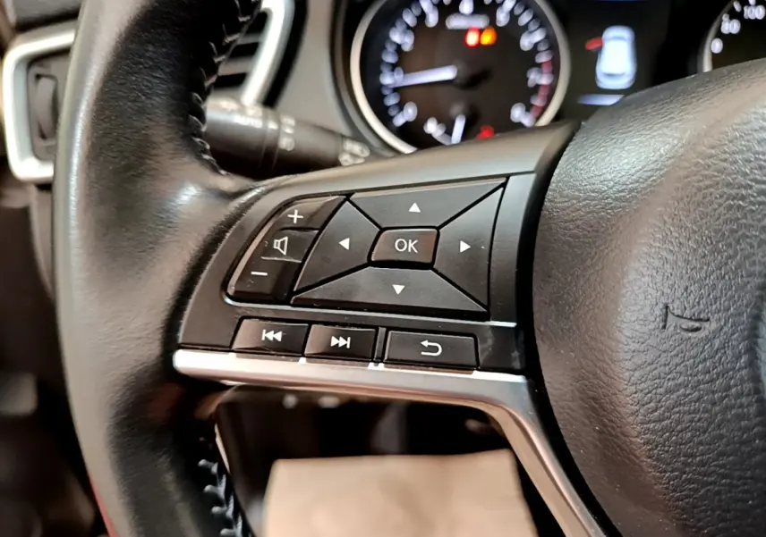 Gros plan sur les commandes multifonctions noires à gauche du volant cuir d’un Nissan Qashqai blanc 2019.