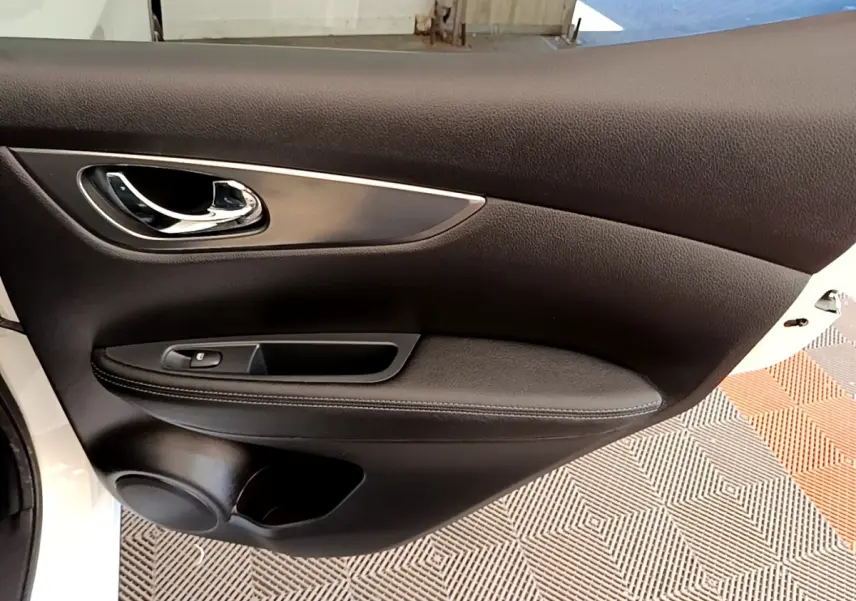 Gros plan sur la porte intérieure côté gauche du Nissan Qashqai blanc, avec poignée chrome et commande de vitre.