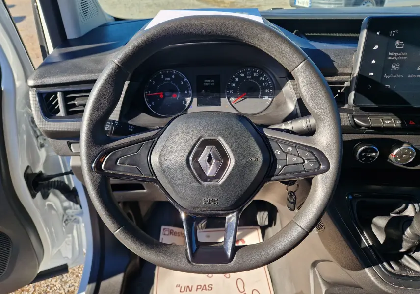 Vue rapprochée du volant noir d’un Renault Kangoo blanc 2023, avec tableau de bord et écran tactile visibles.