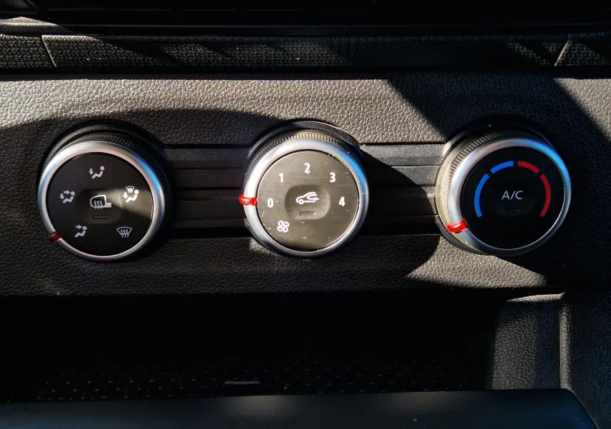 Gros plan sur les commandes de climatisation du Renault Kangoo blanc 2023, avec réglages de ventilation, air recyclé et température.