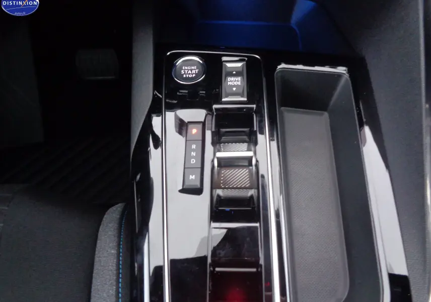 Gros plan sur la console centrale noire brillante du Peugeot 5008 2023 avec bouton start, levier automatique et rangement latéral.