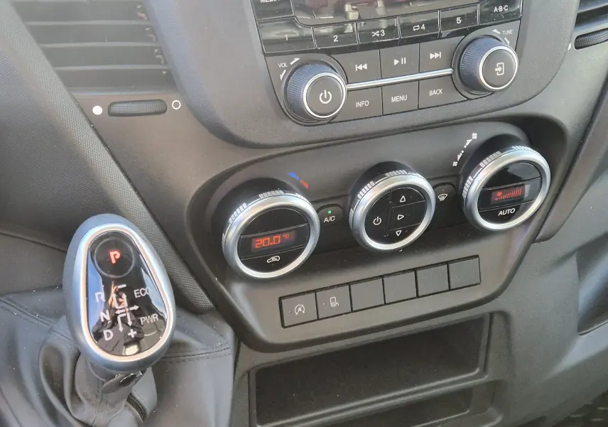 Gros plan sur la console centrale et levier de boîte automatique du fourgon Iveco Daily blanc, avec commandes climatisation numériques.