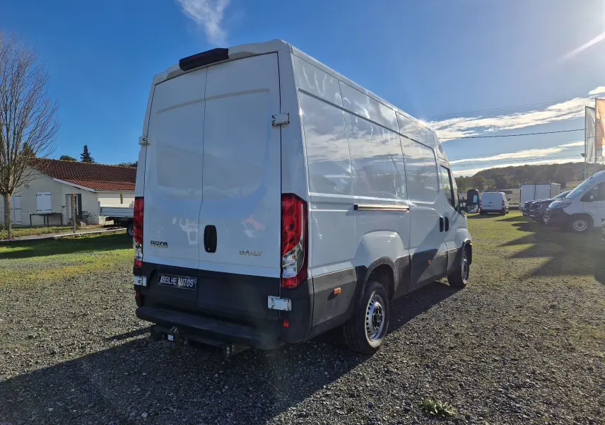 IVECO Daily fourgon blanc vu en 3/4 arrière droit sur un terrain avec attelage et marchepied arrière visible.