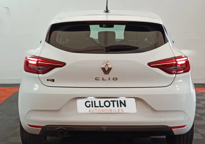 Vue arrière d'une Renault Clio blanche 2021 avec feux LED allumés et logo central visible.