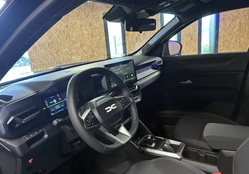 Intérieur du Dacia Duster 1.6 Hybrid 140 Journey 2025 en tissu gris noir, vue côté conducteur avec tableau de bord et écran tactile.