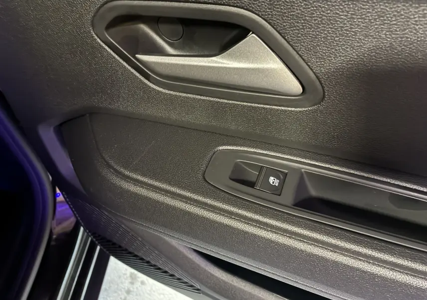 Gros plan sur la poignée intérieure et le bouton de commande de la vitre côté gauche du Dacia Duster 1.6 Hybrid noir 2025.