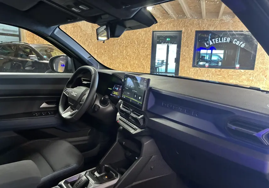 Vue intérieure côté conducteur du Dacia Duster 1.6 Hybrid 140 noir, avec tableau de bord moderne et écran tactile central.