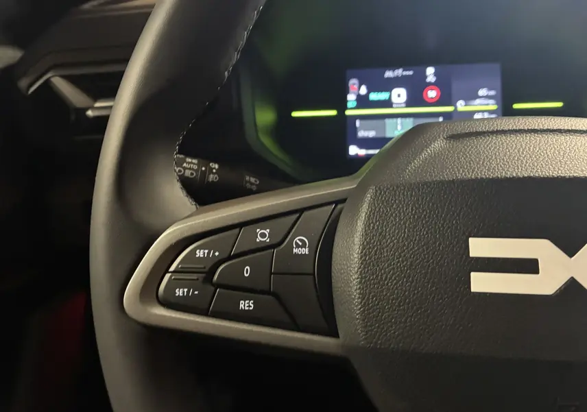 Gros plan sur le volant noir du Dacia Duster 1.6 Hybrid 140 Journey 2025, avec commandes de régulateur et tableau de bord numérique en arrière-plan.