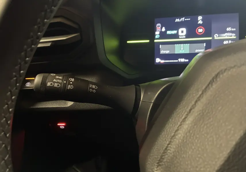 Vue rapprochée du commodo d’éclairage noir à gauche du volant dans un Dacia Duster 2025 avec tableau de bord numérique allumé.