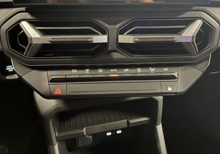 Gros plan sur la console centrale noire du Dacia Duster 2025, avec les aérateurs hexagonaux et les commandes de climatisation.