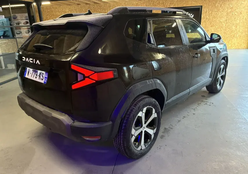 Vue 3/4 arrière droite du Dacia Duster 1.6 Hybrid 140 noir, avec feux arrière en forme de X et jantes bicolores.