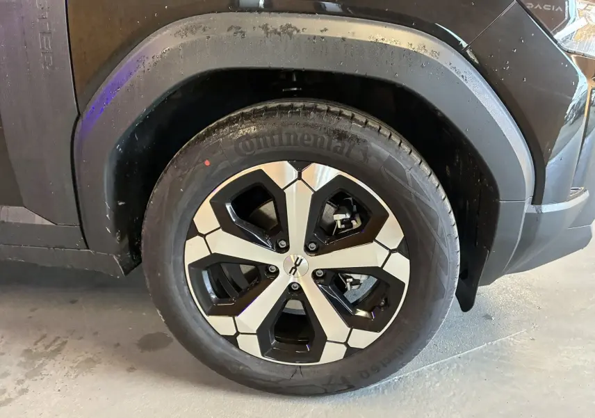 Gros plan sur la roue avant droite du Dacia Duster noir 2025, mettant en valeur la jante bicolore au design géométrique.