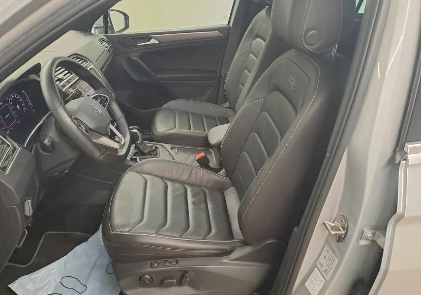 Vue intérieure côté gauche du Volkswagen Tiguan 2024 argent, avec sièges avant en cuir noir et volant multifonction.
