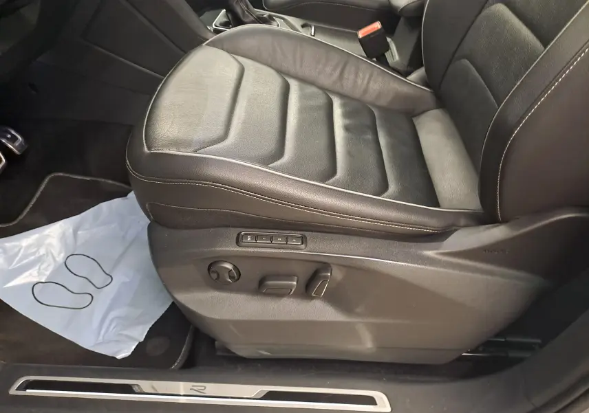 Vue rapprochée du siège avant gauche en cuir noir du Volkswagen Tiguan 2024, avec réglages électriques et surpiqûres claires.
