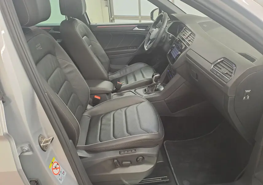 Vue intérieure côté conducteur du Volkswagen Tiguan 2024 argent, sièges cuir noirs R-Line avec commandes électriques.