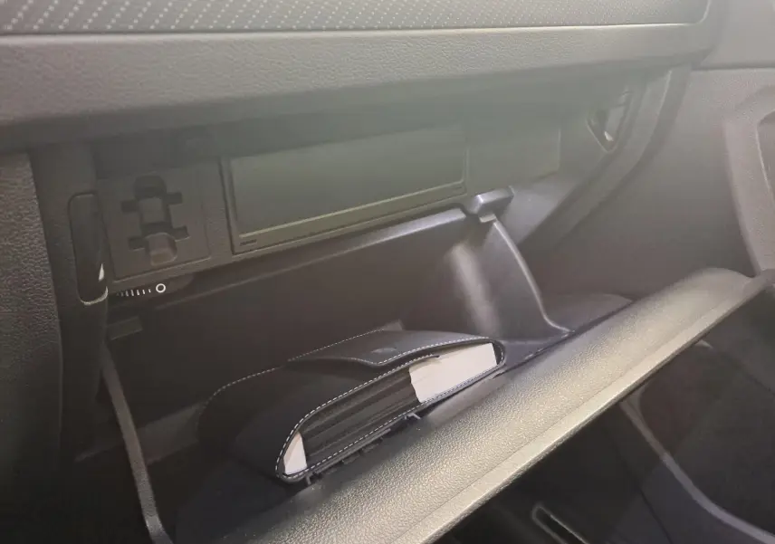Gros plan de la boîte à gants ouverte du Volkswagen Tiguan 2024, avec un carnet noir à l'intérieur, intérieur noir.