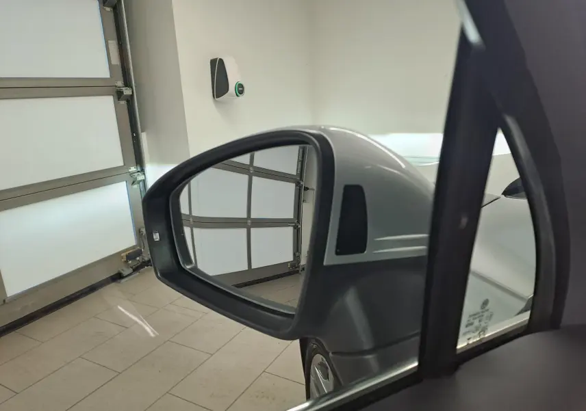 Rétroviseur côté gauche d'un Volkswagen Tiguan 2024 argenté, avec reflet de porte de garage en arrière-plan.
